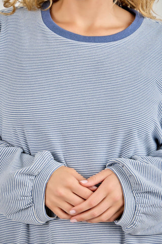 Close-up of a person wearing a blue and white striped shirt with hands clasped in front.