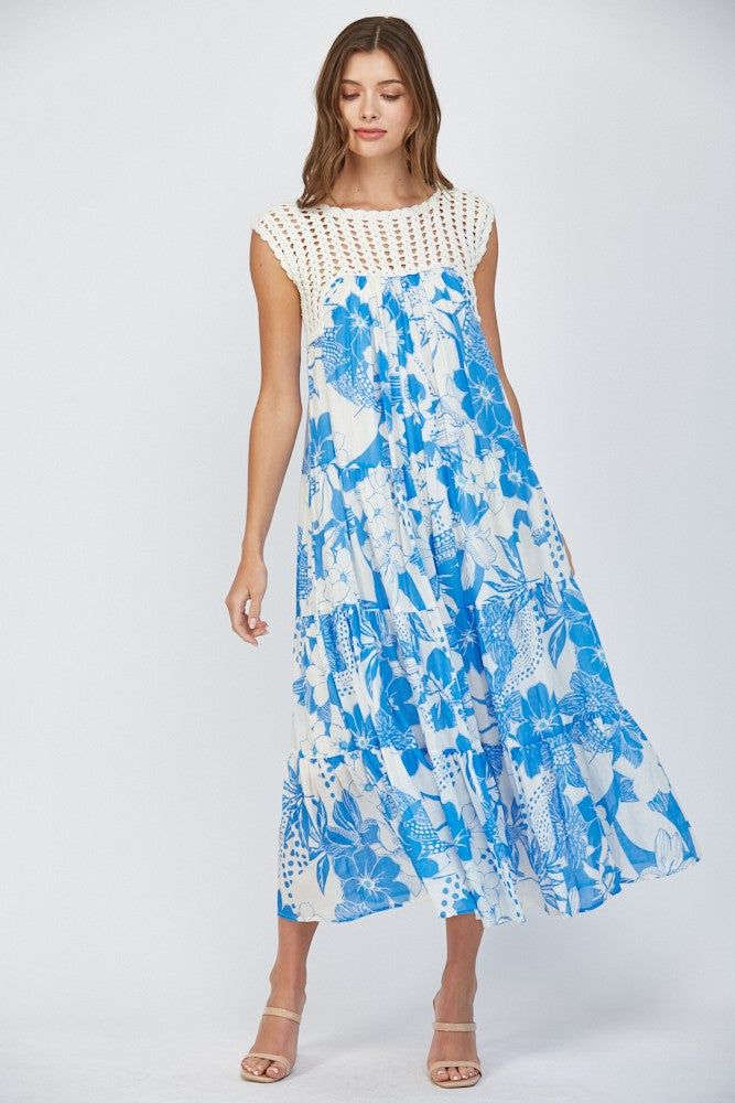 Women wearing a floral blue dress with crochet sleeves on a white background.