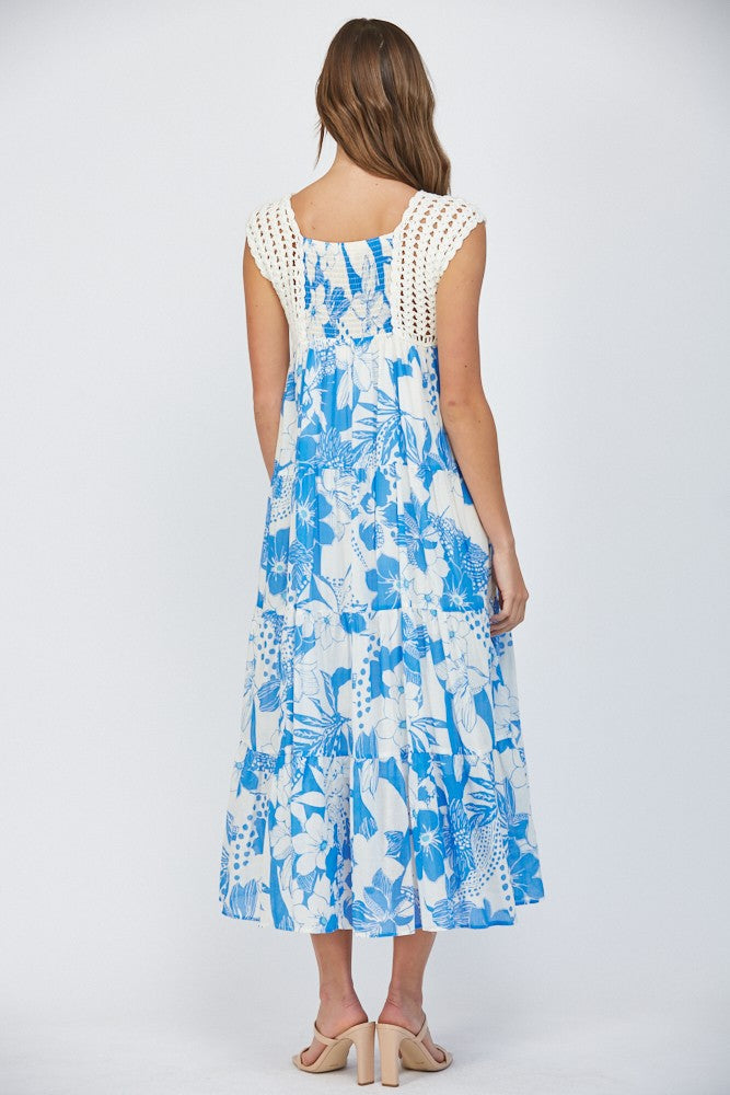 Women wearing a floral blue dress with crochet sleeves on a white background.