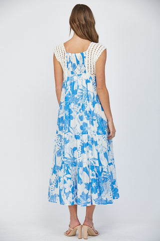 Women wearing a floral blue dress with crochet sleeves on a white background.