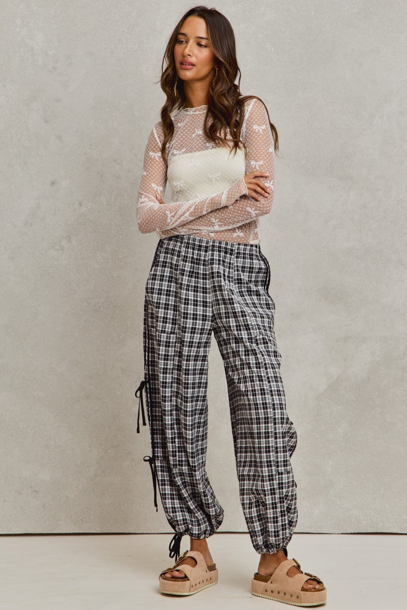 Woman wearing a sheer top and plaid pants against a plain background