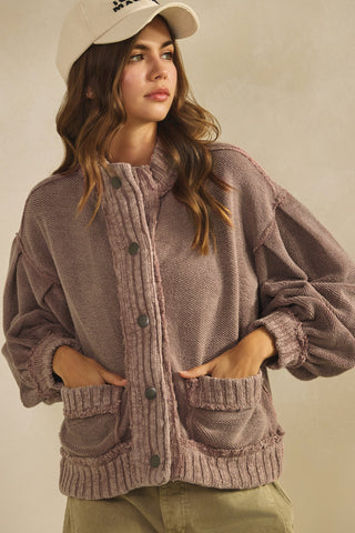 Woman wearing a purple cardigan with a beige cap on a neutral background