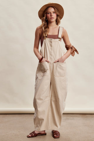 Woman wearing beige overalls and a straw hat on a plain background