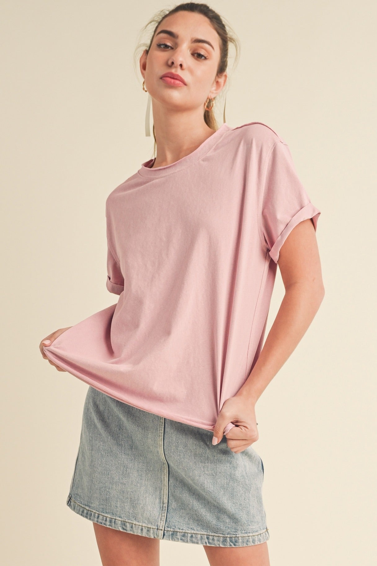 Woman wearing a pink oversized t-shirt and denim skirt on a beige background