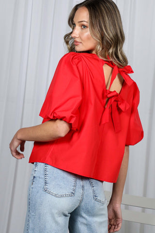 Woman wearing a red blouse with bow details and light blue jeans against a white background