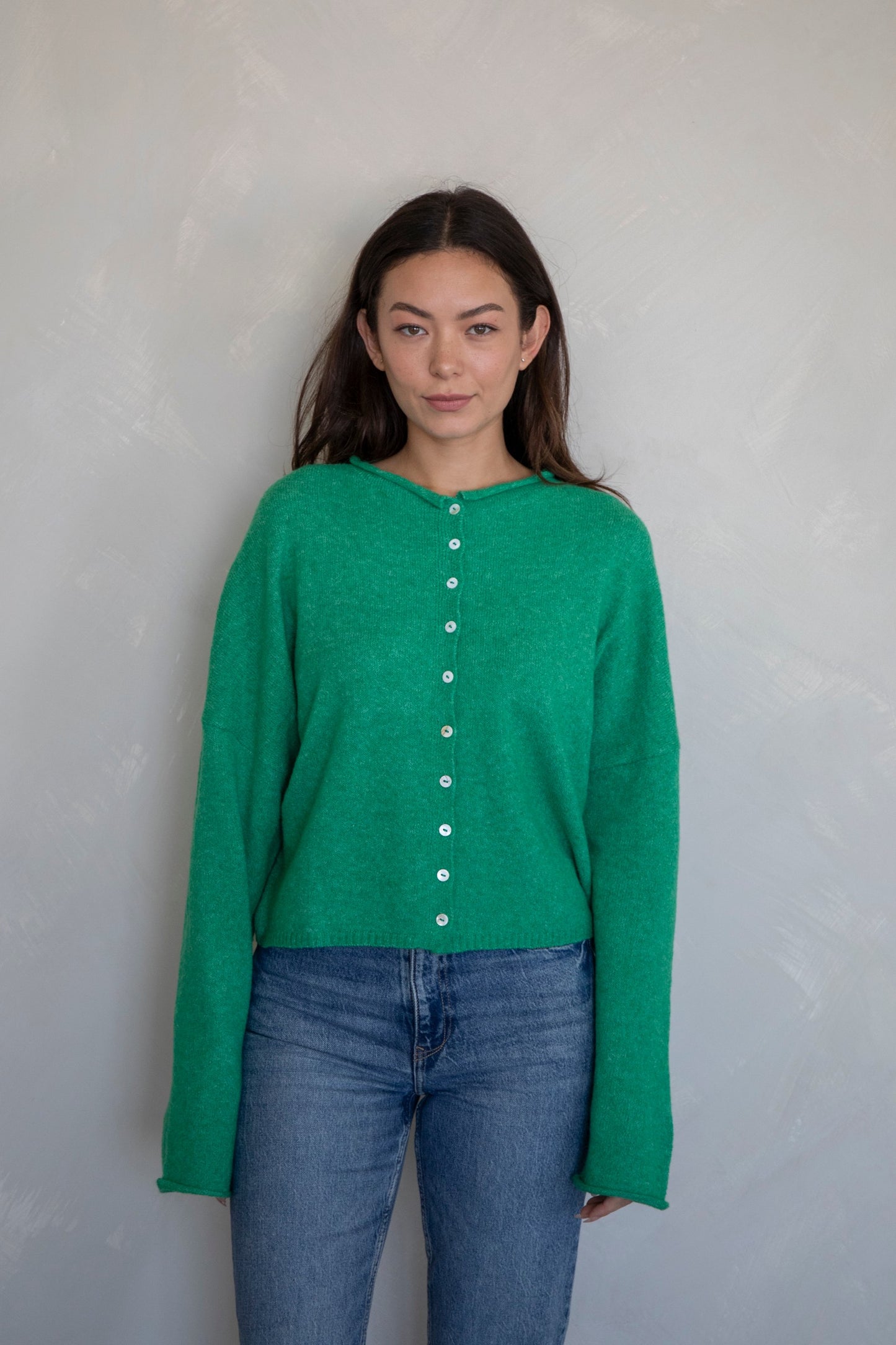 Woman wearing a green long-sleeve shirt with buttons and blue jeans against a plain background