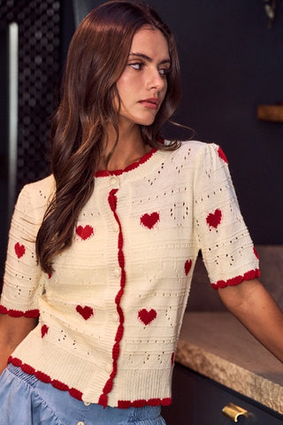 Woman wearing a cream cardigan with red heart patterns