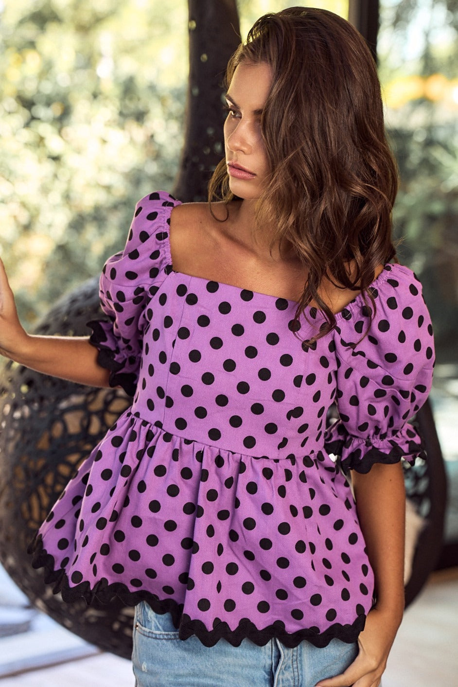 Woman wearing a purple polka dot blouse with puffed sleeves outdoors.