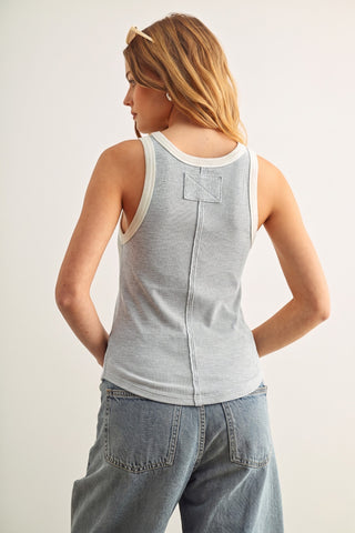 A woman shown from the back wearing a light heather gray sleeveless tank top with white trim and a small square patch detail on the upper back, paired with light blue jeans against a plain light background.