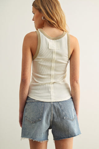 A woman shown from the back wearing a cream ribbed tank top with beige trim and light-wash denim shorts against a plain light background.