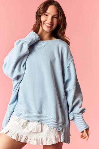 Women wearing a blue oversized sweater against a pink background. 