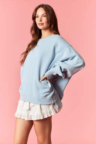 Women wearing a blue oversized sweater against a pink background. 