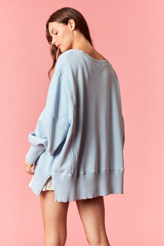 Women wearing a blue oversized sweater against a pink background. 