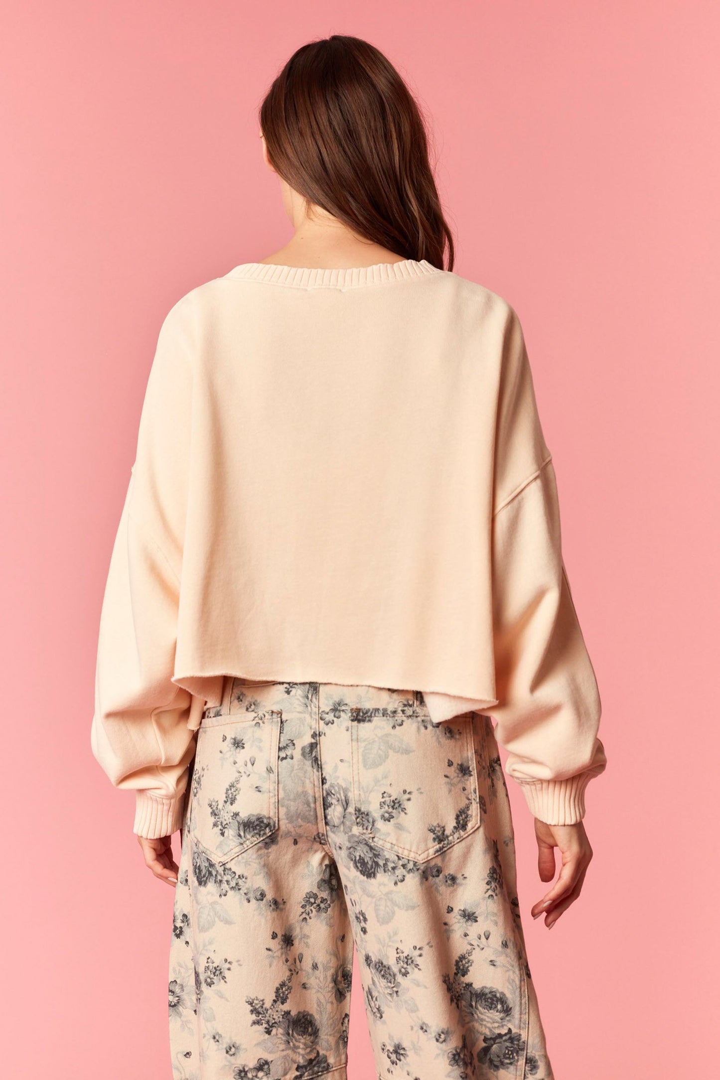 Person wearing a light orange sweater and floral pants against a pink background