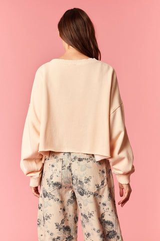Person wearing a light orange sweater and floral pants against a pink background