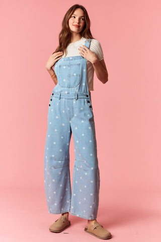 Women wearing polka dot overalls against a pink background.