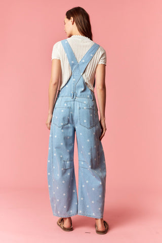 Women wearing polka dot overalls against a pink background.