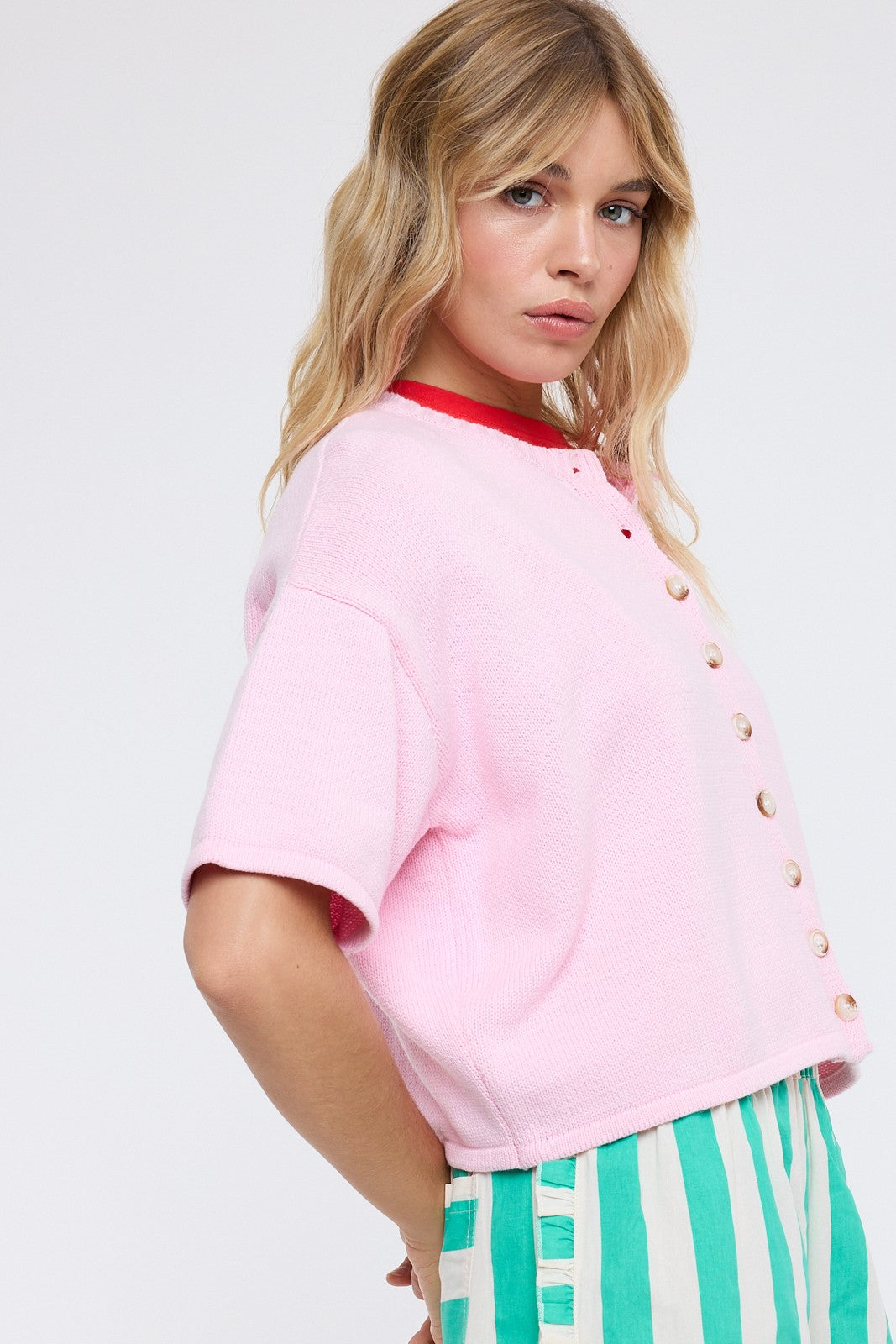 Woman wearing a pink cardigan with a red collar and striped pants on a white background