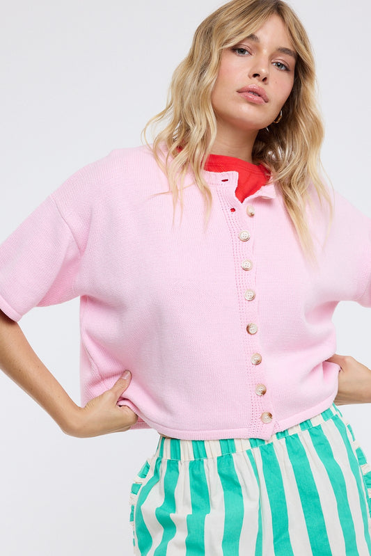 Woman wearing a pink cardigan over a red shirt with green and white striped pants on a white background