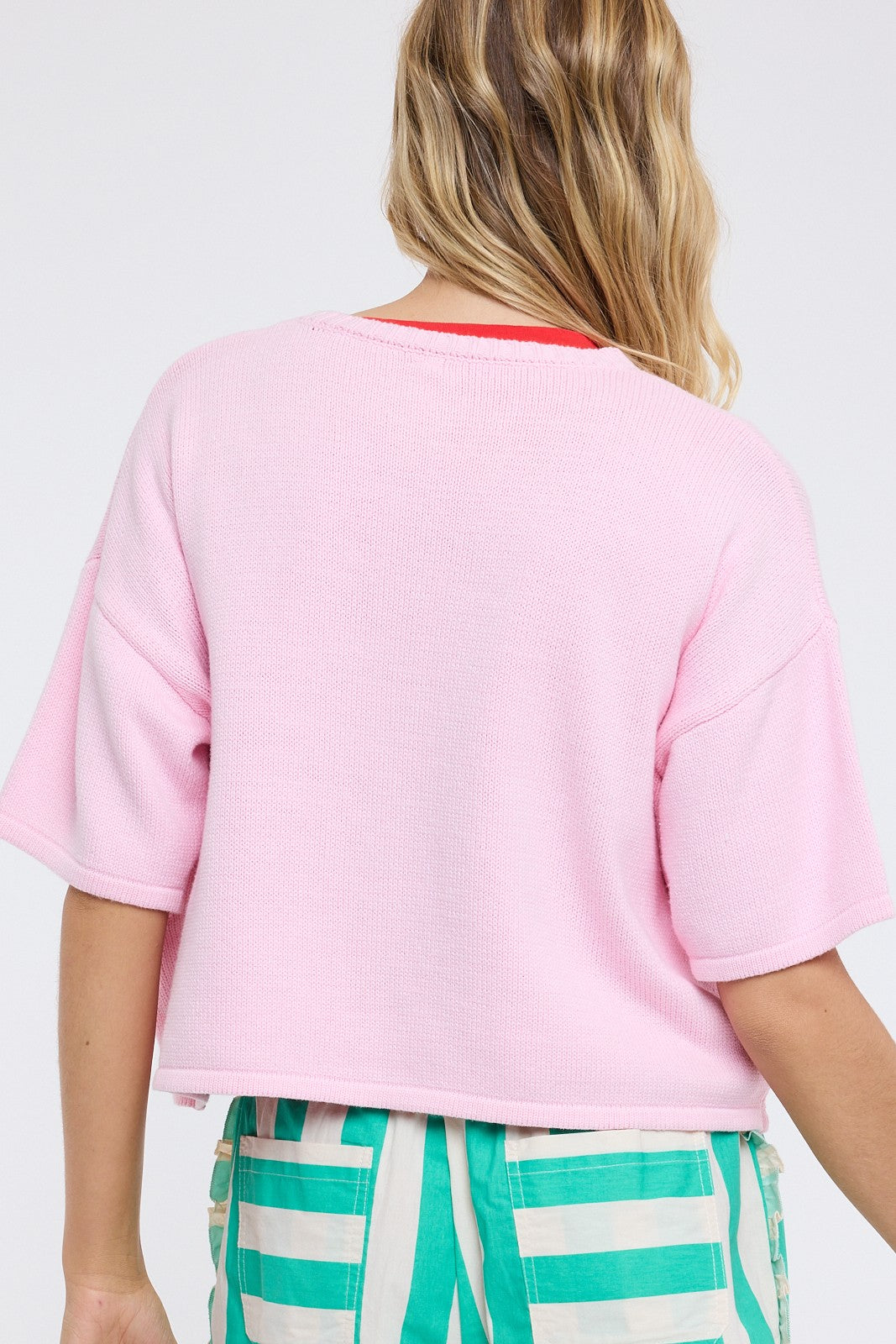 Person wearing a pink crop top and green striped pants on a white background