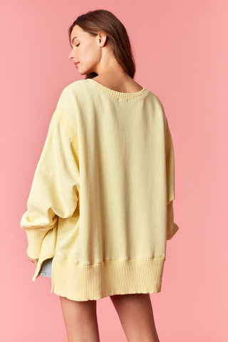 Women wearing a yellow oversized sweater against a pink background. 