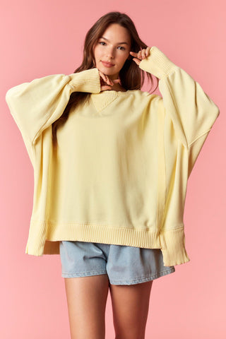 Women wearing a yellow oversized sweater against a pink background. 