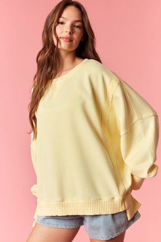 Women wearing a yellow oversized sweater against a pink background. 