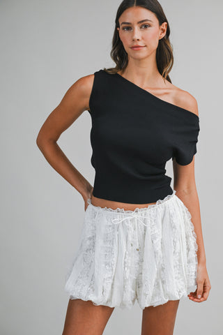Woman wearing a black one-shoulder top and white lace skirt on a gray background