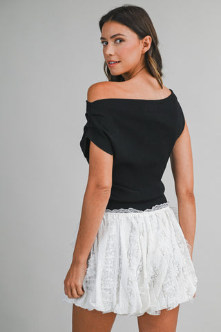 Woman wearing a black off-shoulder top and white lace skirt on a gray background