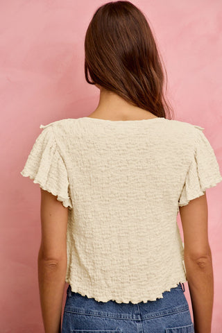Woman wearing a textured beige top against a pink background