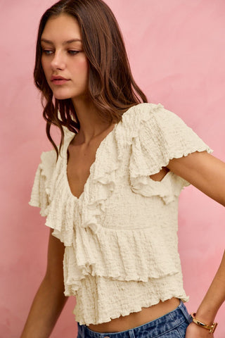 Woman wearing a white ruffled top against a pink background