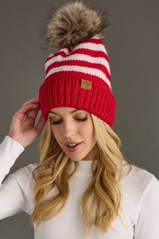 Person wearing a red and white striped beanie with a pom-pom on a gray background