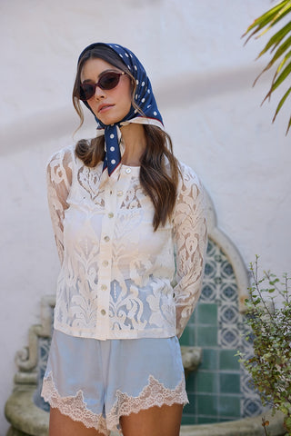 Woman wearing a lace outfit with a blue headscarf in an outdoor setting