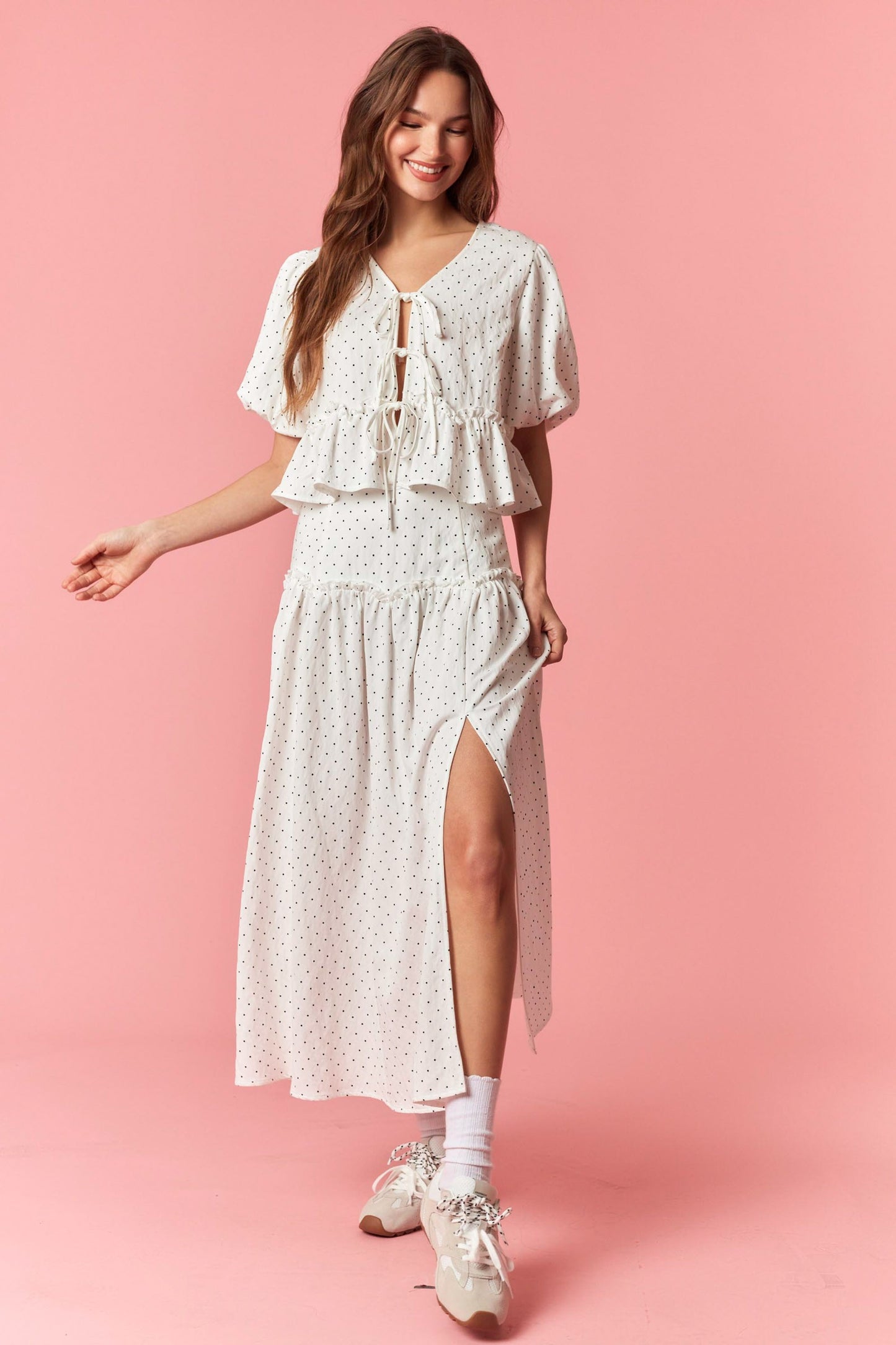 Woman wearing a white floral dress with a slit on a pink background
