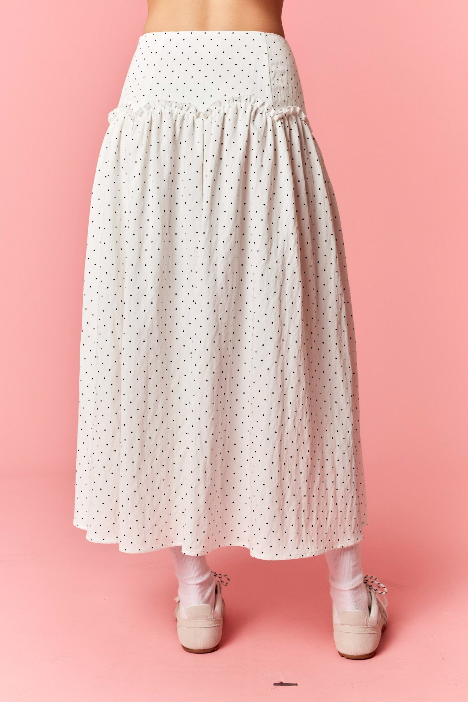 White polka dot skirt worn by a person on a pink background