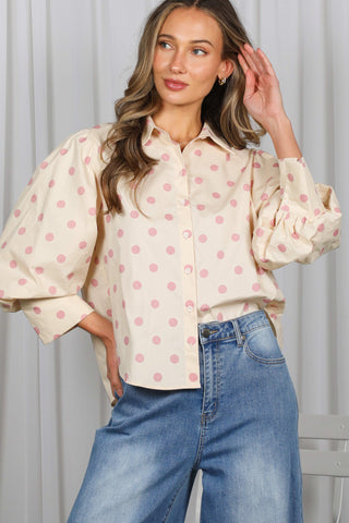 Woman wearing a cream blouse with pink polka dots and blue jeans against a white background