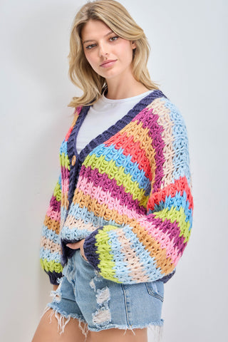 Woman wearing a colorful crocheted cardigan against a plain background