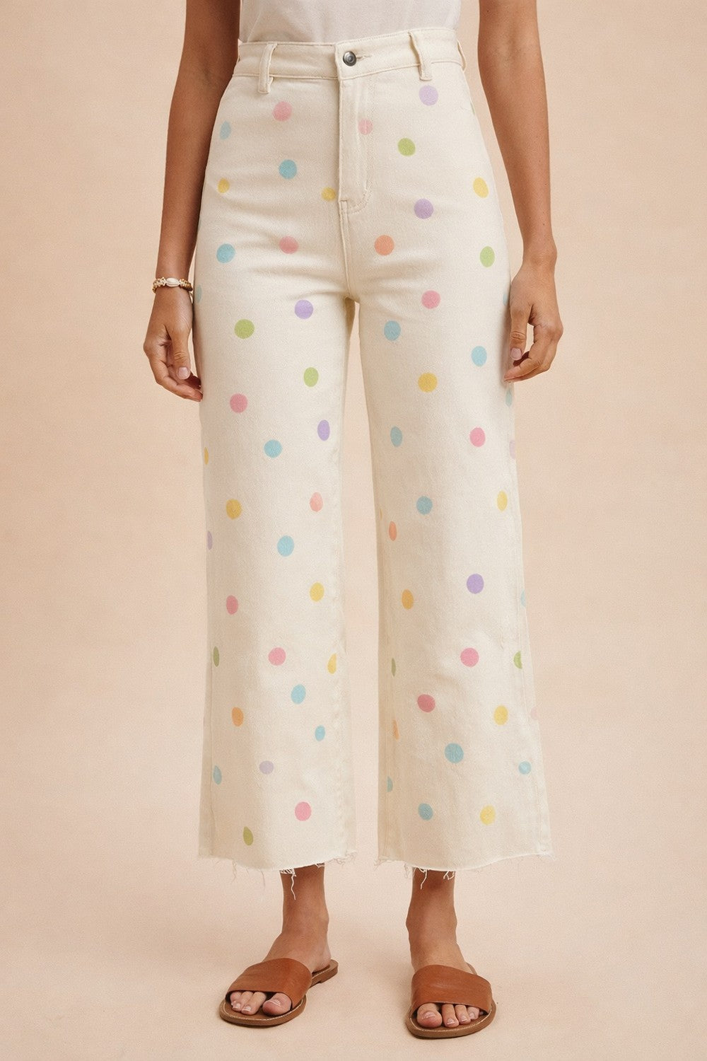 White pants with colorful polka dots worn by a person on a beige background