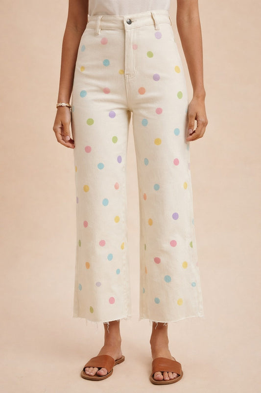 White pants with colorful polka dots worn by a person on a beige background