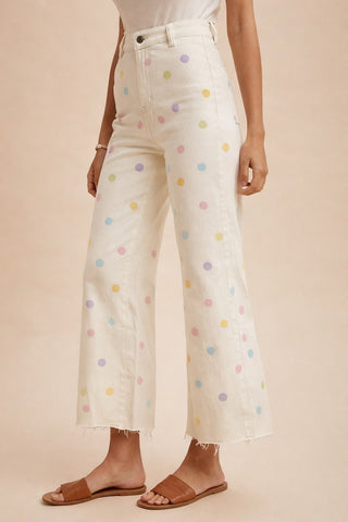 White jeans with colorful polka dots worn by a person on a beige background