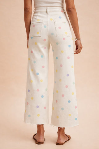 Person wearing white pants with colorful polka dots on a beige background