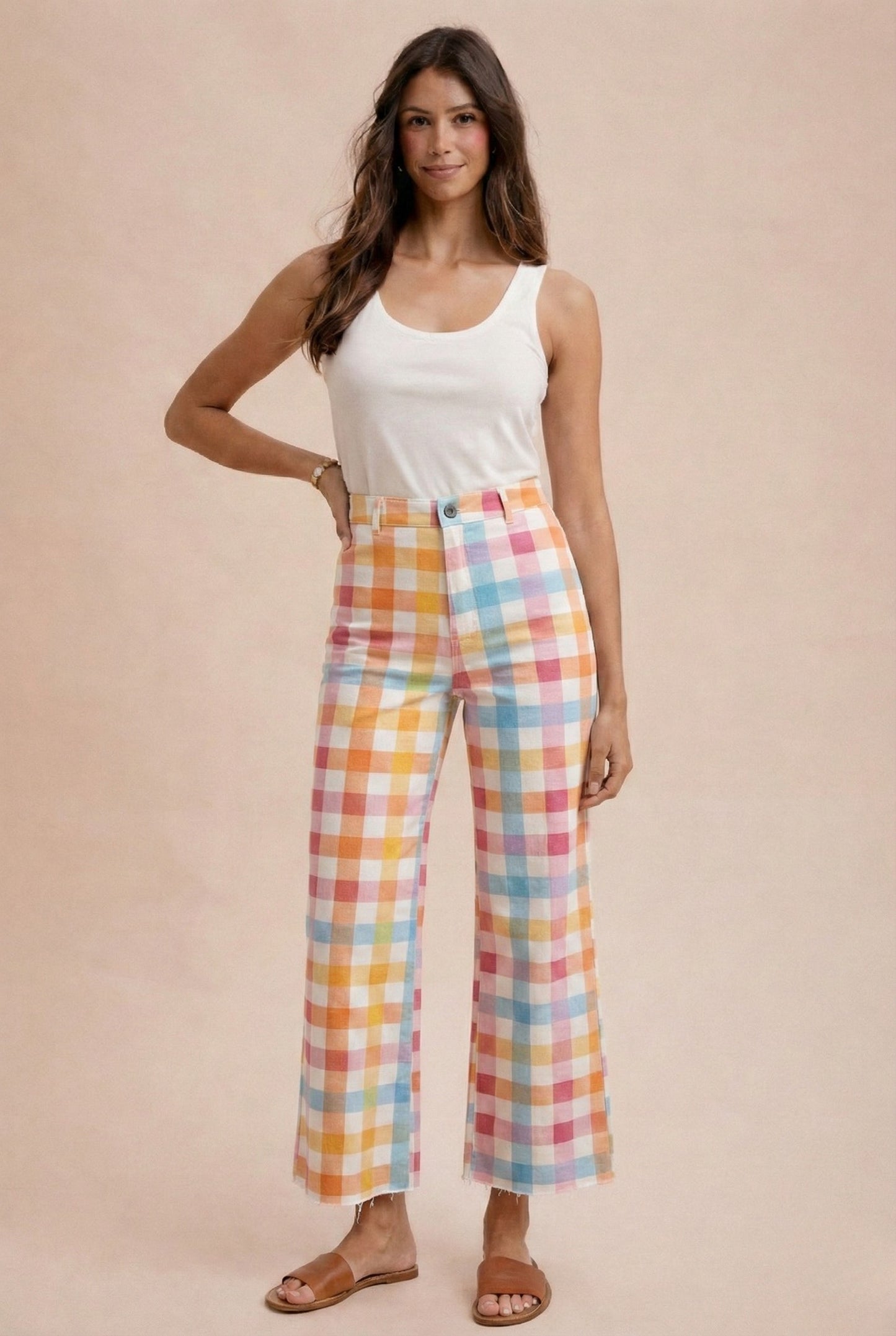 Woman wearing a white tank top and colorful plaid pants on a beige background
