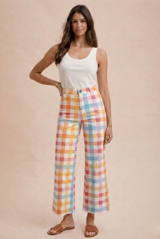 Woman wearing a white tank top and colorful plaid pants on a beige background