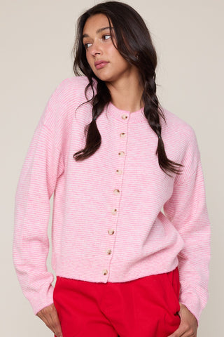 Woman wearing a pink cardigan with gold buttons against a plain background