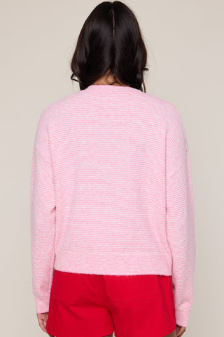 Person wearing a pink textured cardiganand red pants on a plain background