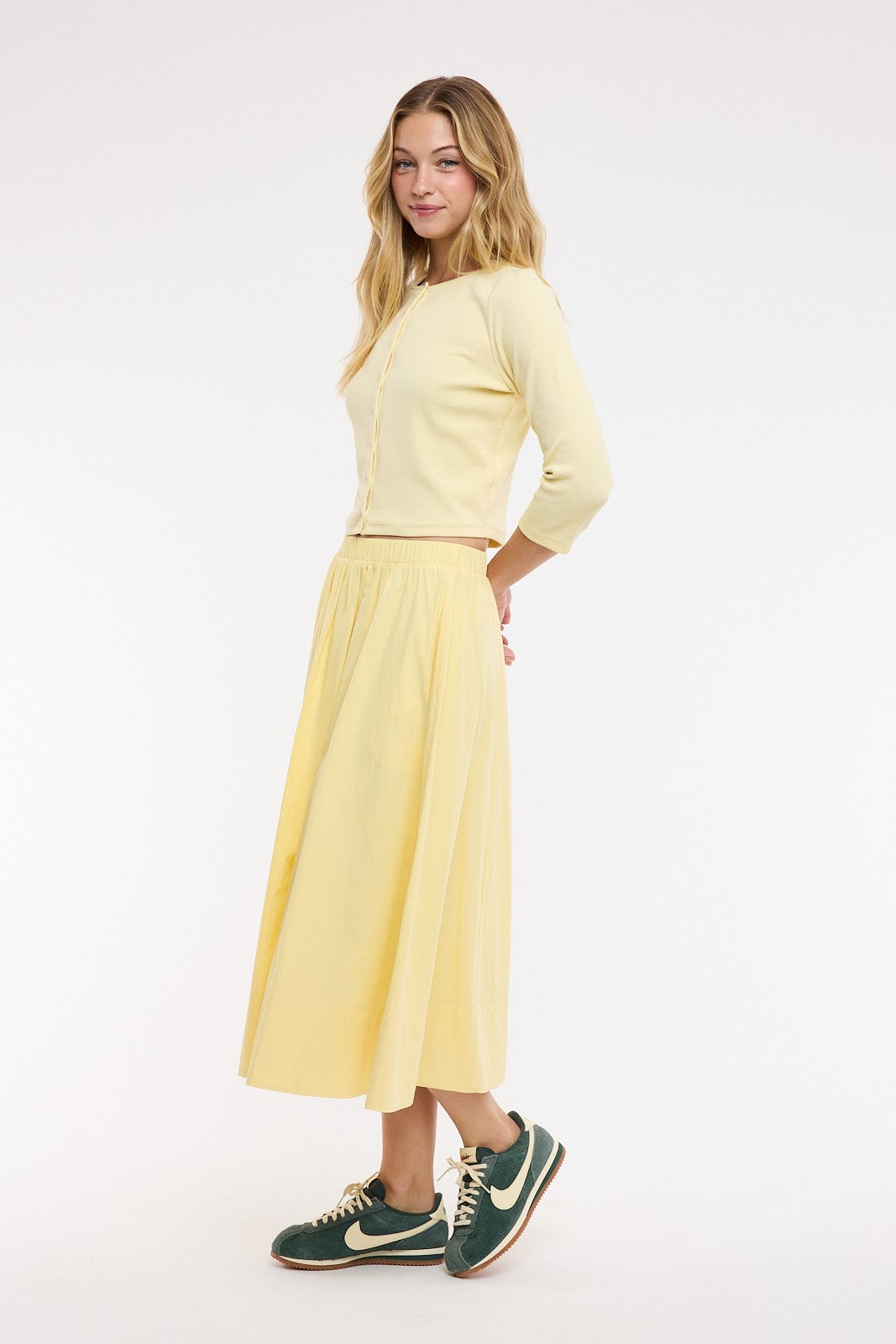 Woman wearing a light yellow outfit with a skirt and sneakers on a white background
