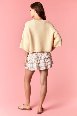 Woman wearing a beige top and patterned shorts on a pink background