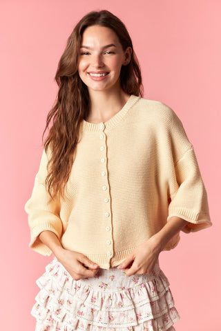 Woman wearing a light yellow cardigan over a floral dress on a pink background
