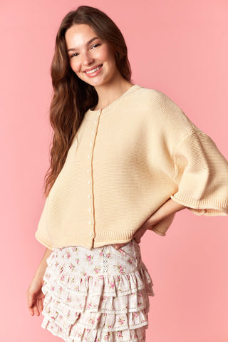 Woman wearing a light yellow cardigan over a floral skirt on a pink background