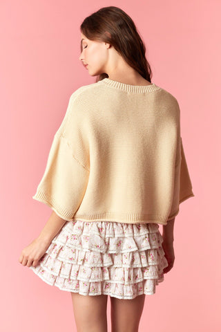 Woman wearing a beige poncho and floral skirt against a pink background